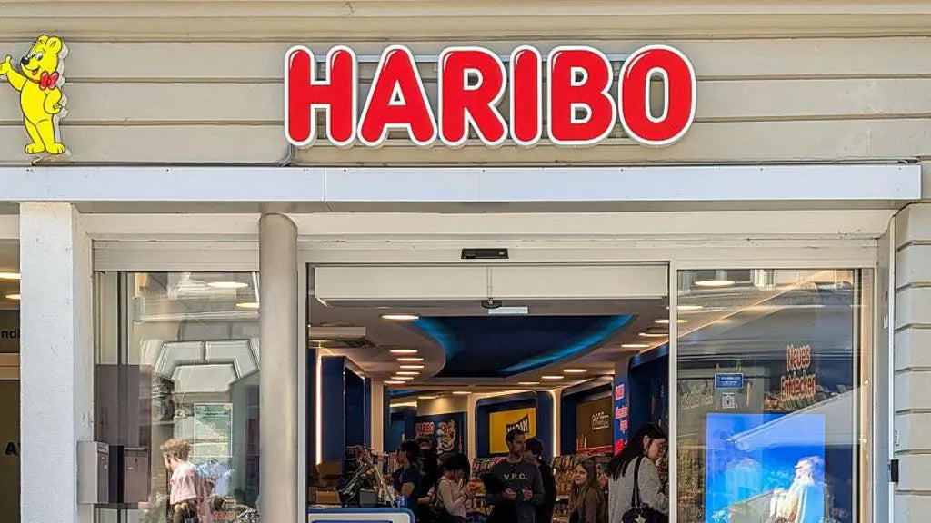 Fachada de uma loja Haribo, com o nome da marca em letras vermelhas e clientes no interior.