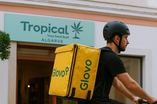 Estafeta da Glovo a entregar produtos de CBD da Tropical Bud em Albufeira, Algarve, com mochila amarela, em frente a loja de cânhamo. Entregas rápidas, seguras e discretas de flores e óleos de CBD.